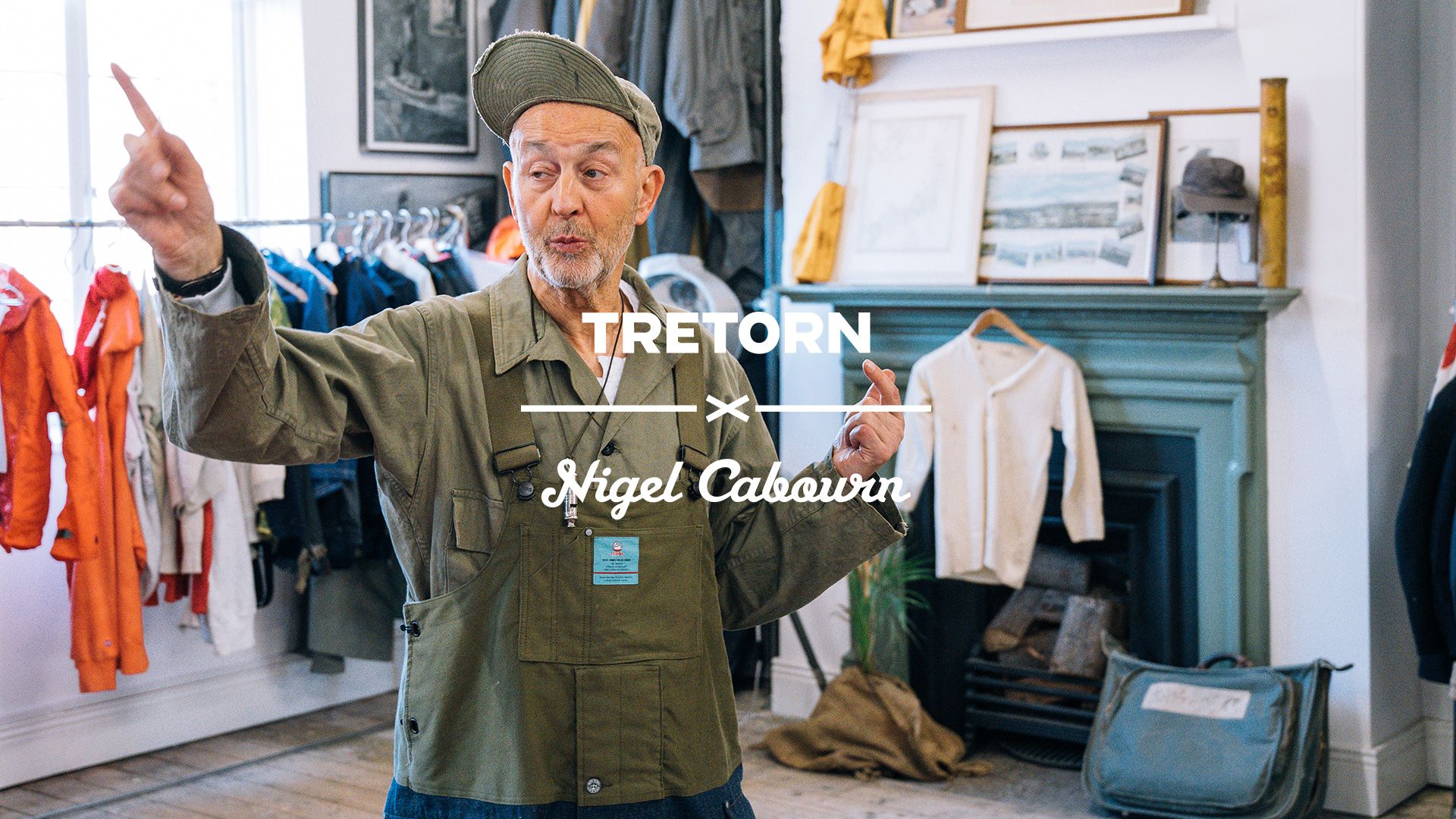 Man in a green jacket and cap gestures in a clothing store, with orange jackets and framed photos in the background. Text reads "Tretorn x Nigel Cabourn."
