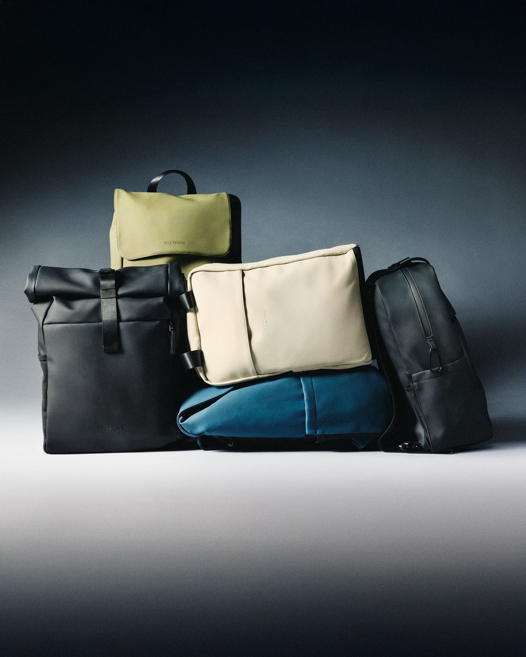 A collection of five stylish bags in various colors, including black, beige, olive, and blue, arranged against a dark gradient background.
