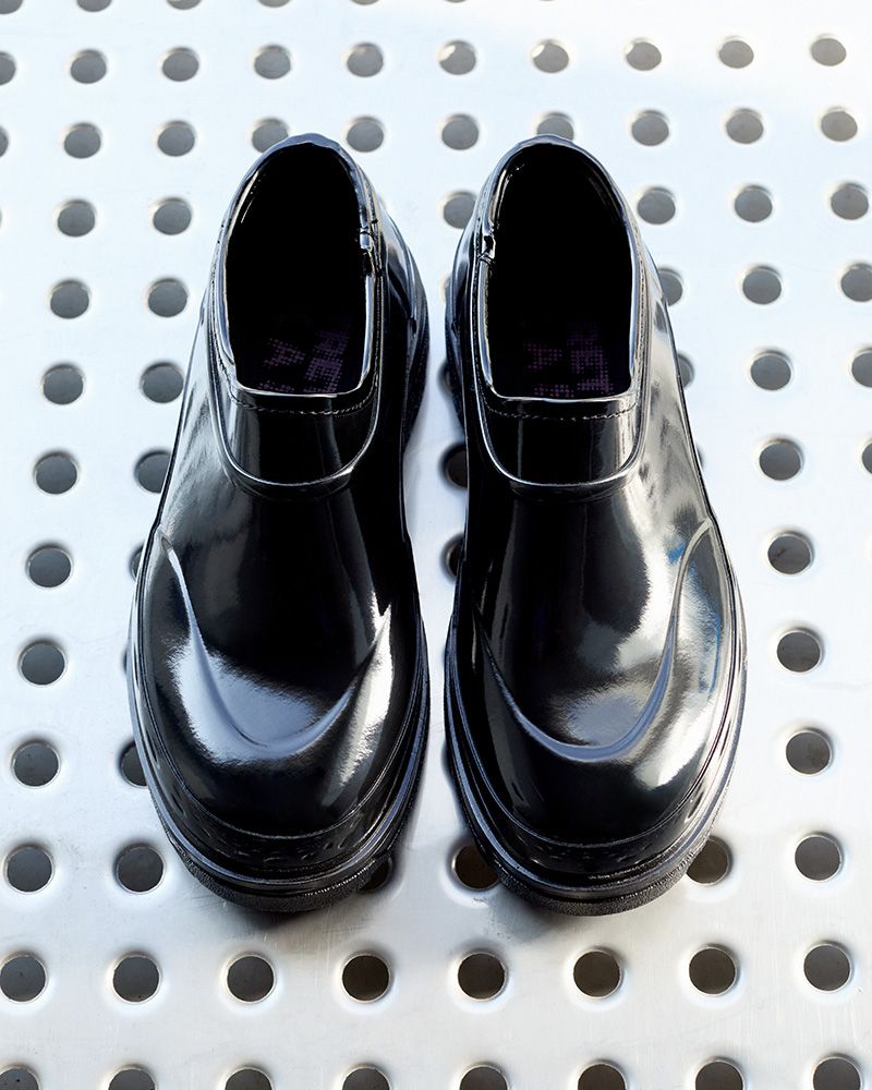 Shiny black ankle boots on a perforated metal surface, viewed from above.