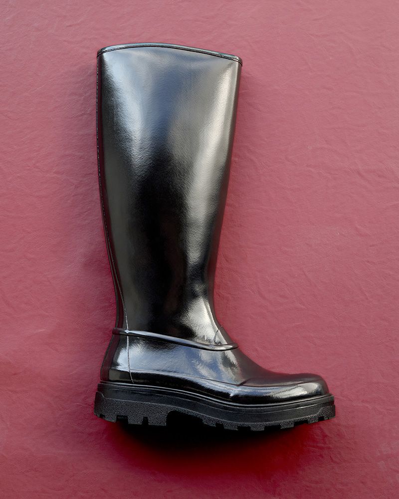Shiny black knee-high boot with a chunky sole, displayed on a textured red background.