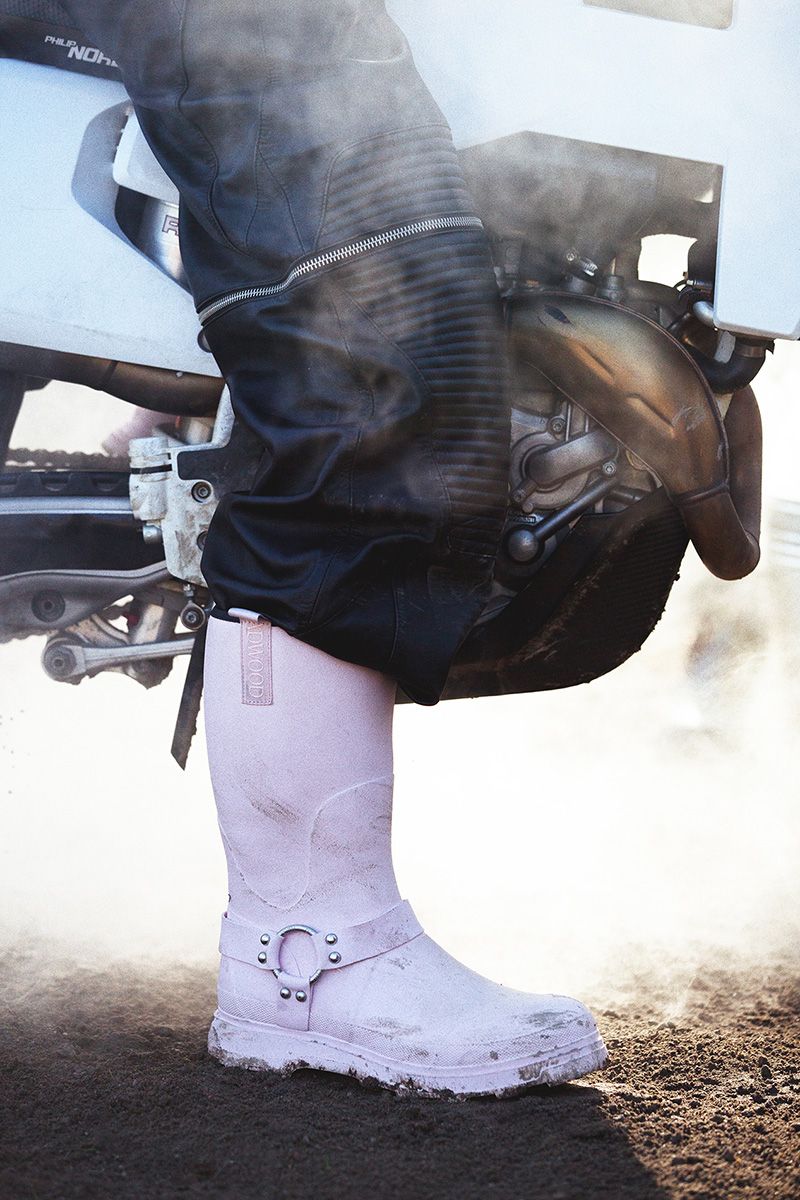 Person in leather pants and pink boots standing next to a motorcycle, with steam rising around them.